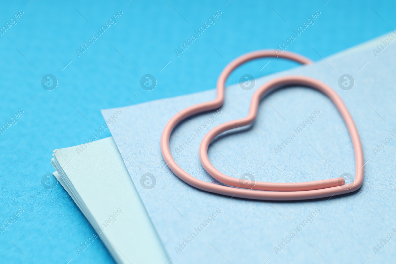 Photo of Heart shaped paper clip and notes on light blue background, closeup