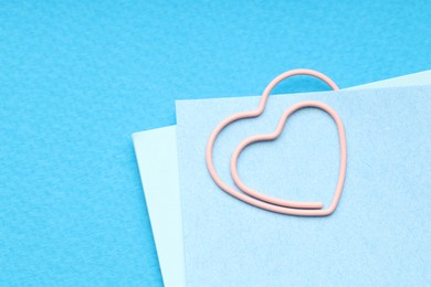 Photo of Heart shaped paper clip and notes on light blue background, top view. Space for text