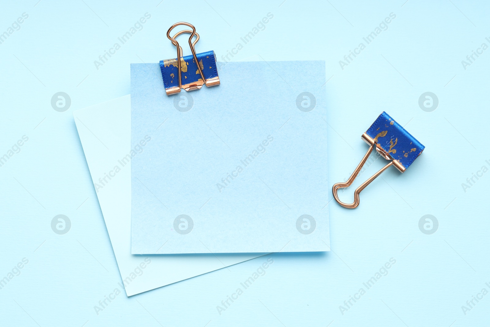 Photo of Binder clips and notes on light blue background, flat lay. Space for text