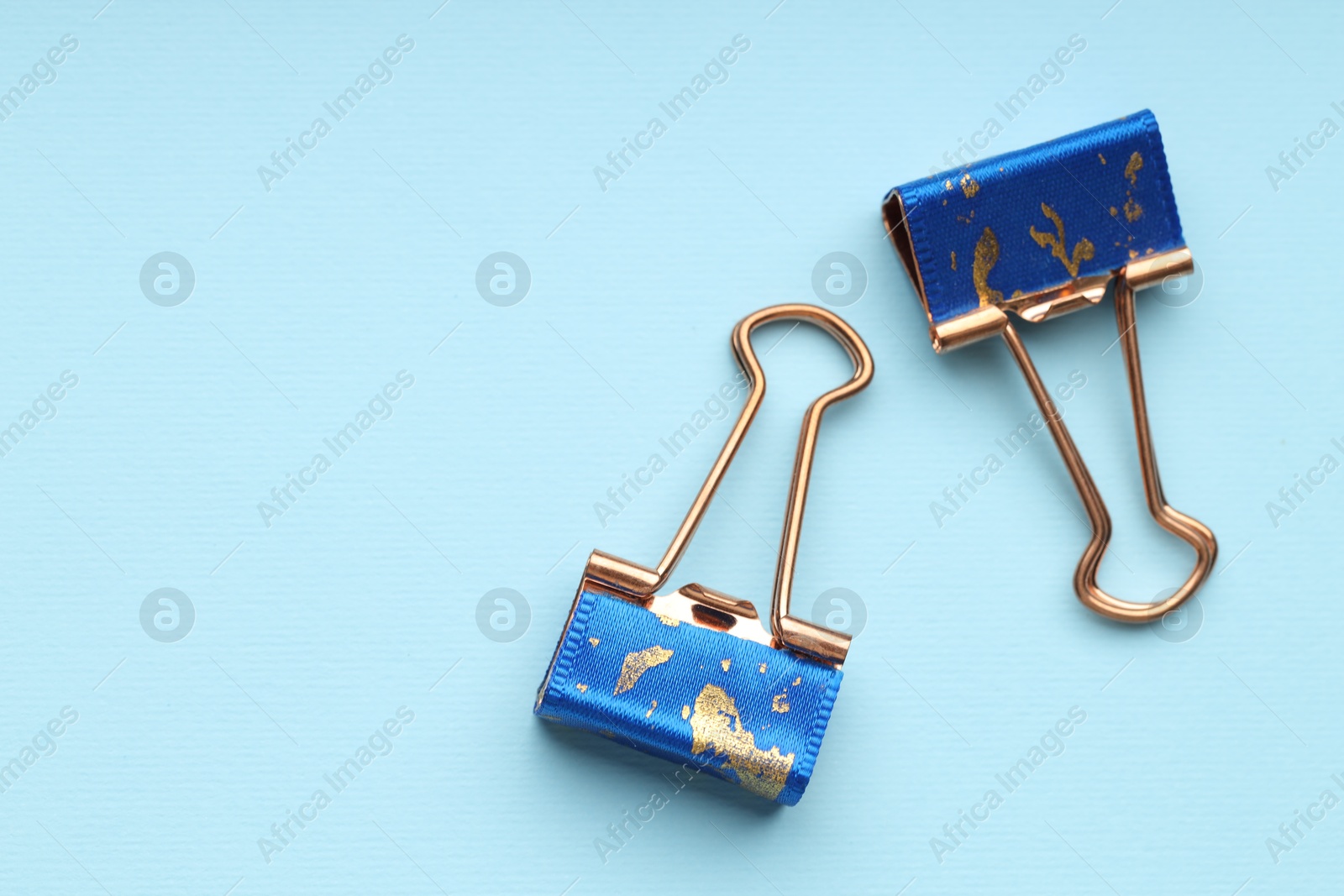 Photo of Two binder clips on light blue background, flat lay. Space for text