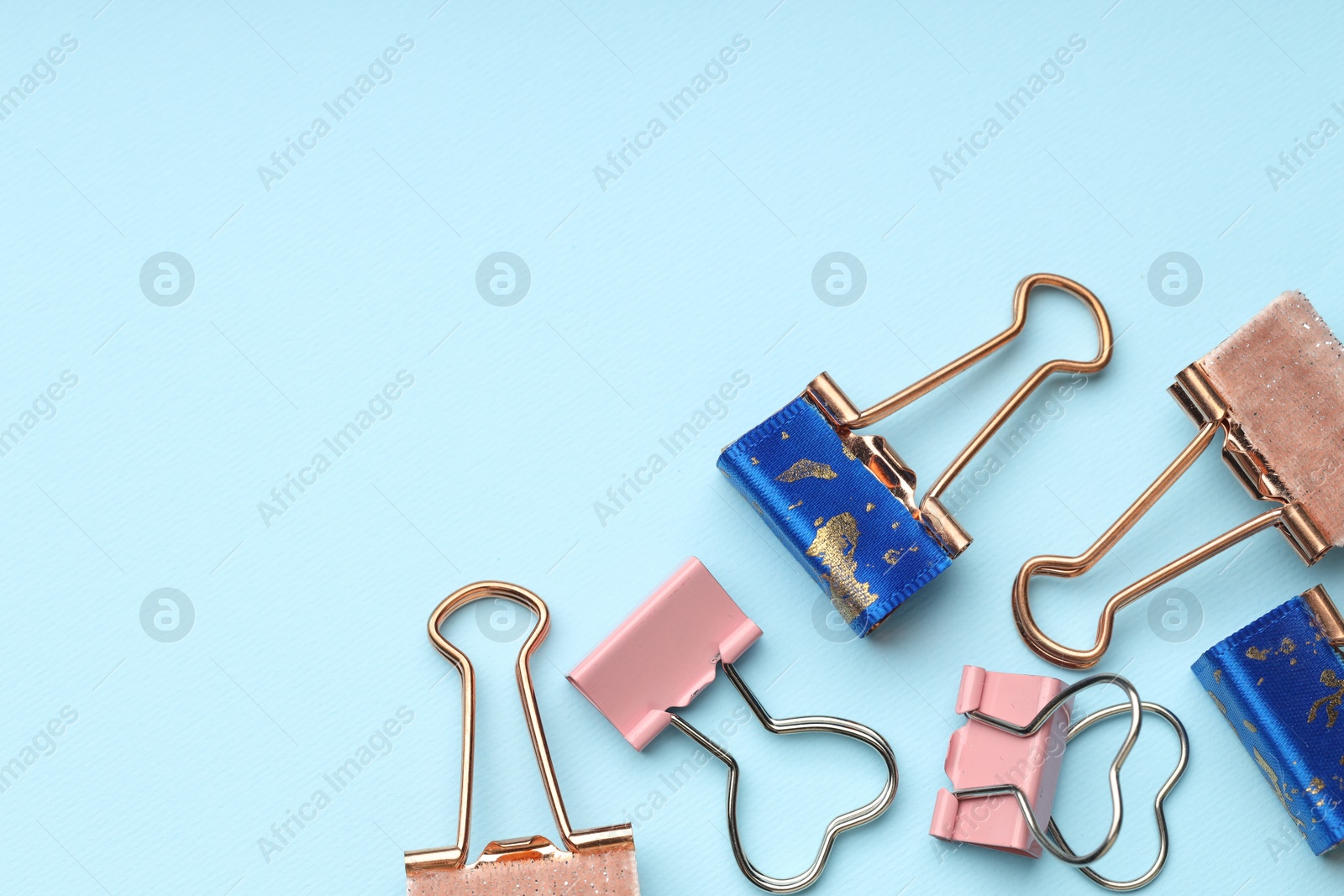 Photo of Different binder clips on light blue background, flat lay. Space for text