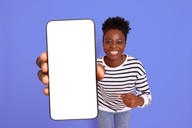 Image of Happy woman pointing at mobile phone with blank screen on violet blue background. Mockup for design