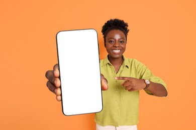 Image of Happy woman pointing at mobile phone with blank screen on orange background. Mockup for design