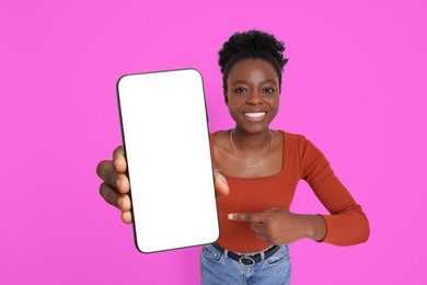 Image of Happy woman pointing at mobile phone with blank screen on magenta color background. Mockup for design