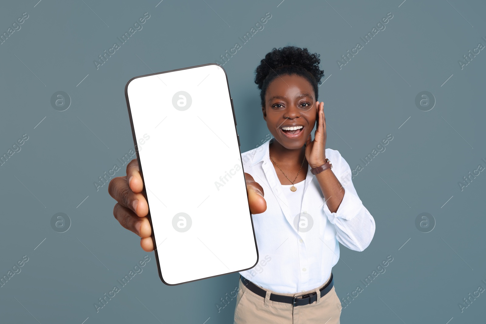 Image of Excited woman showing mobile phone with blank screen on grey background. Mockup for design