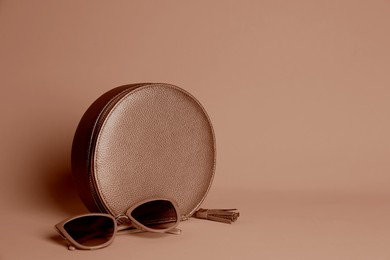 Image of Stylish women's bag in mocha mousse shade and sunglasses on dark beige background. Trendy color of 2025 year