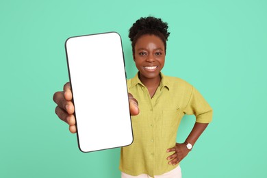 Image of Happy woman showing mobile phone with blank screen on aquamarine color background. Mockup for design