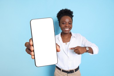 Image of Happy woman pointing at mobile phone with blank screen on light blue background. Mockup for design