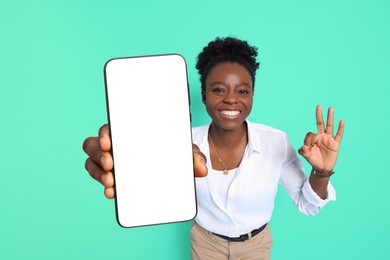 Image of Happy woman showing mobile phone with blank screen and gesture ok on turquoise background. Mockup for design