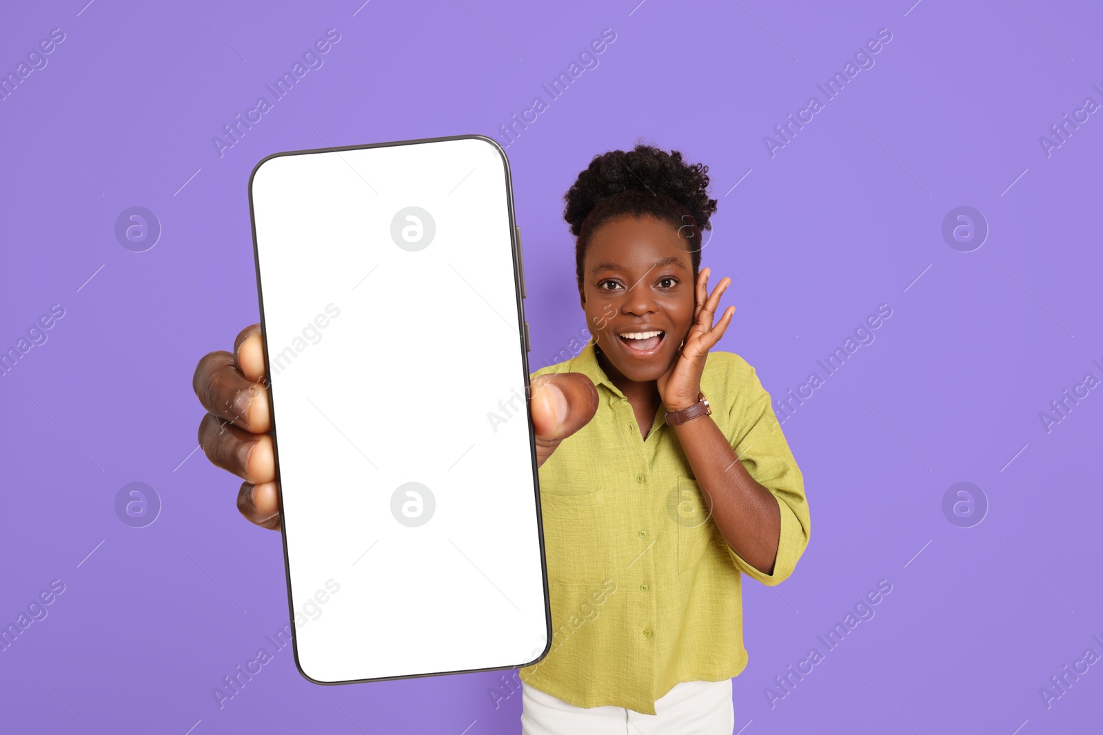 Image of Excited woman showing mobile phone with blank screen on blue violet background. Mockup for design