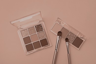 Image of Eyeshadow palettes in mocha mousse shades and makeup brushes on dark beige background, flat lay. Trendy color of 2025 year