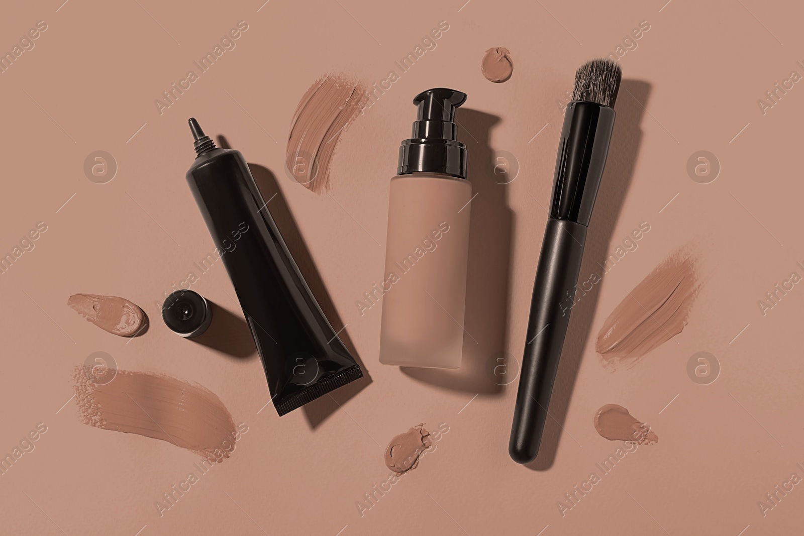 Image of Liquid foundations in mocha mousse shades and makeup brush on dark beige background, flat lay. Trendy color of 2025 year