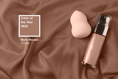 Image of Mocha mousse - trendy color of 2025 year. Liquid foundation and makeup sponge on brown shade fabric, top view