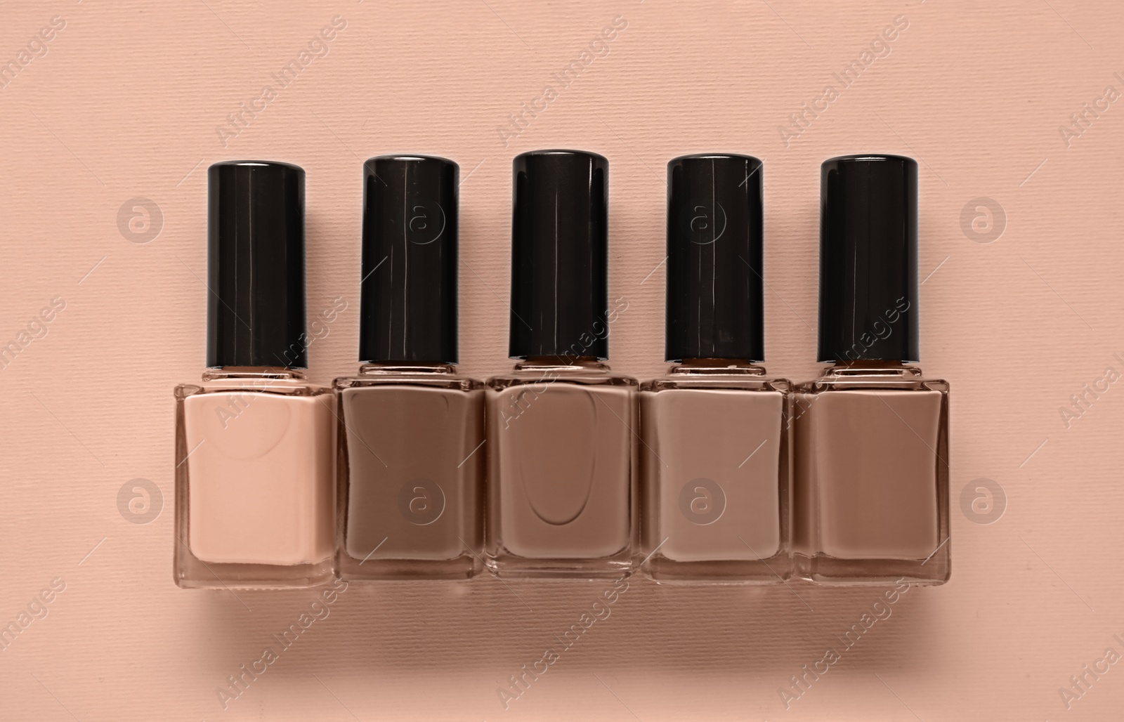 Image of Nail polishes of mocha mousse shades on dark beige background, top view. Trendy color of 2025 year