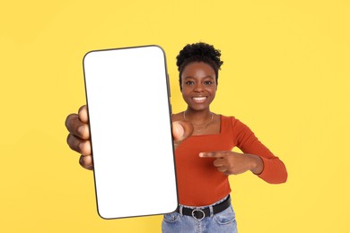 Image of Happy woman pointing at mobile phone with blank screen on yellow background. Mockup for design