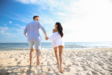 Photo of Happy couple running together on beach, back view