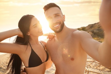 Happy young couple taking selfie on beach at sunset