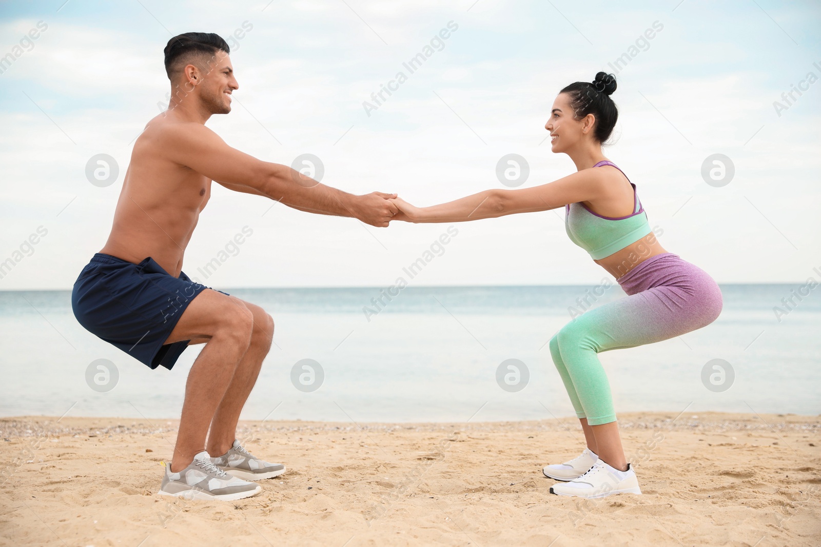 Photo of Couple doing exercise together on beach. Body training