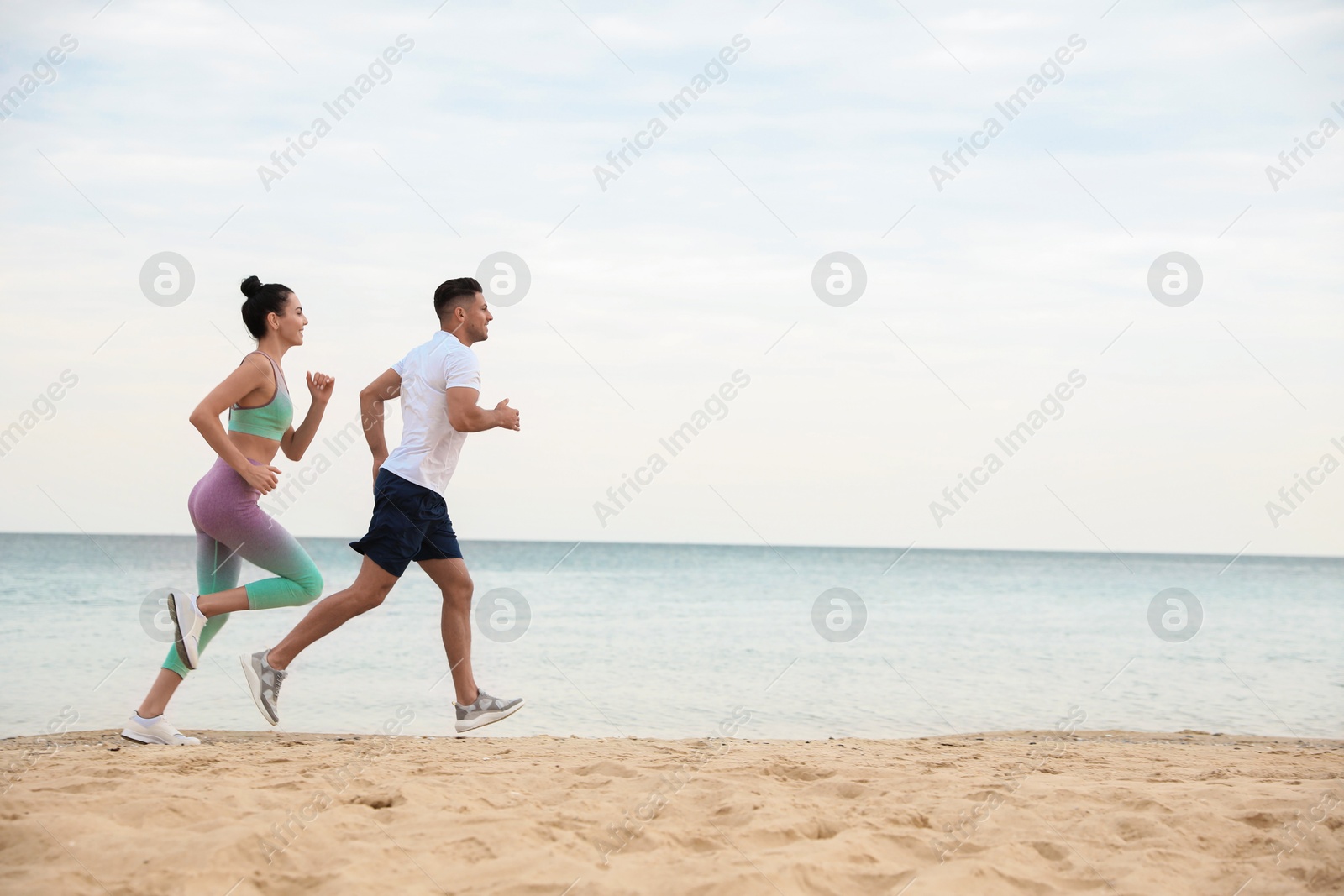 Photo of Couple running together on beach, space for text. Body training