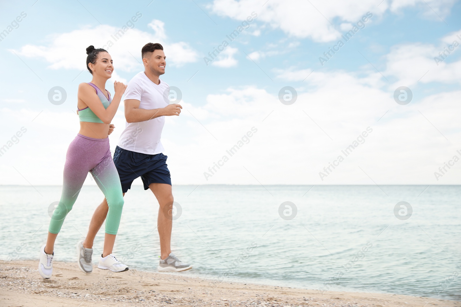 Photo of Couple running together on beach, space for text. Body training