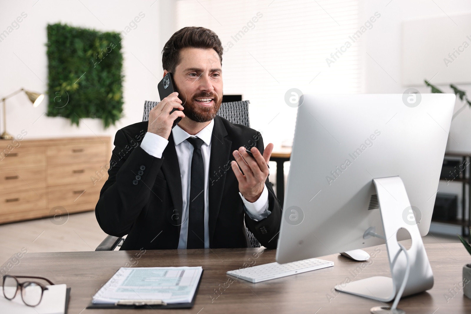 Photo of Man talking on smartphone while working at table in office