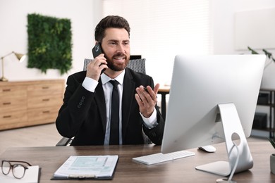 Photo of Man talking on smartphone while working at table in office