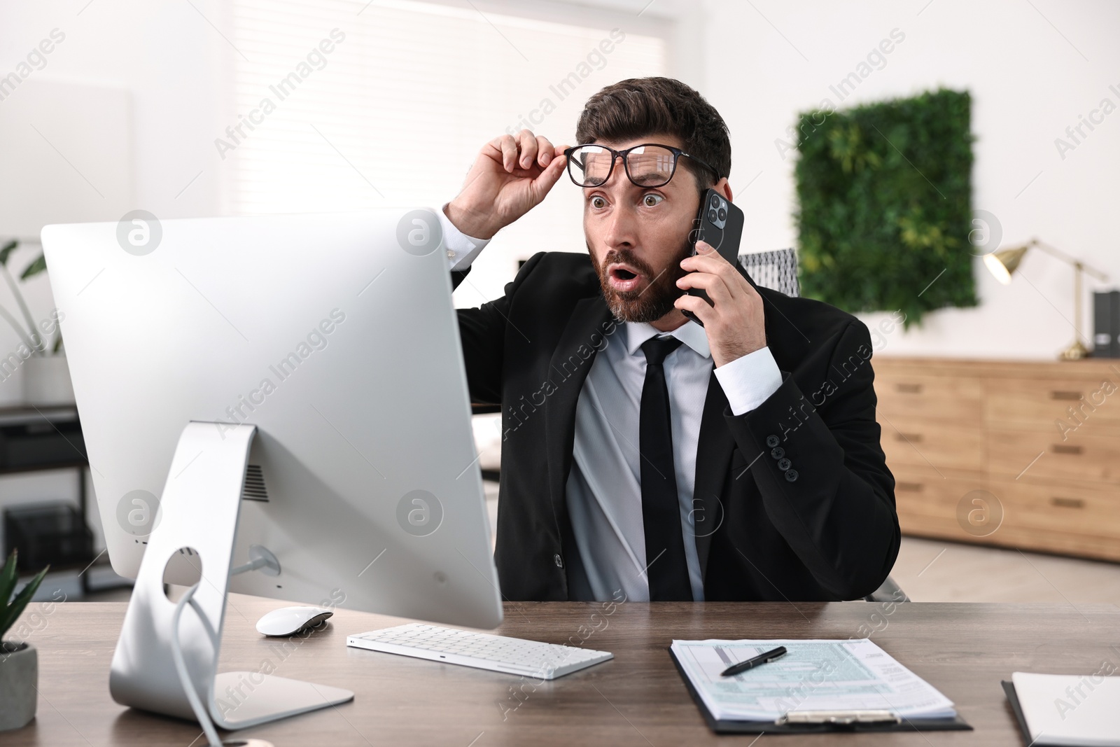 Photo of Man talking on smartphone while working at table in office