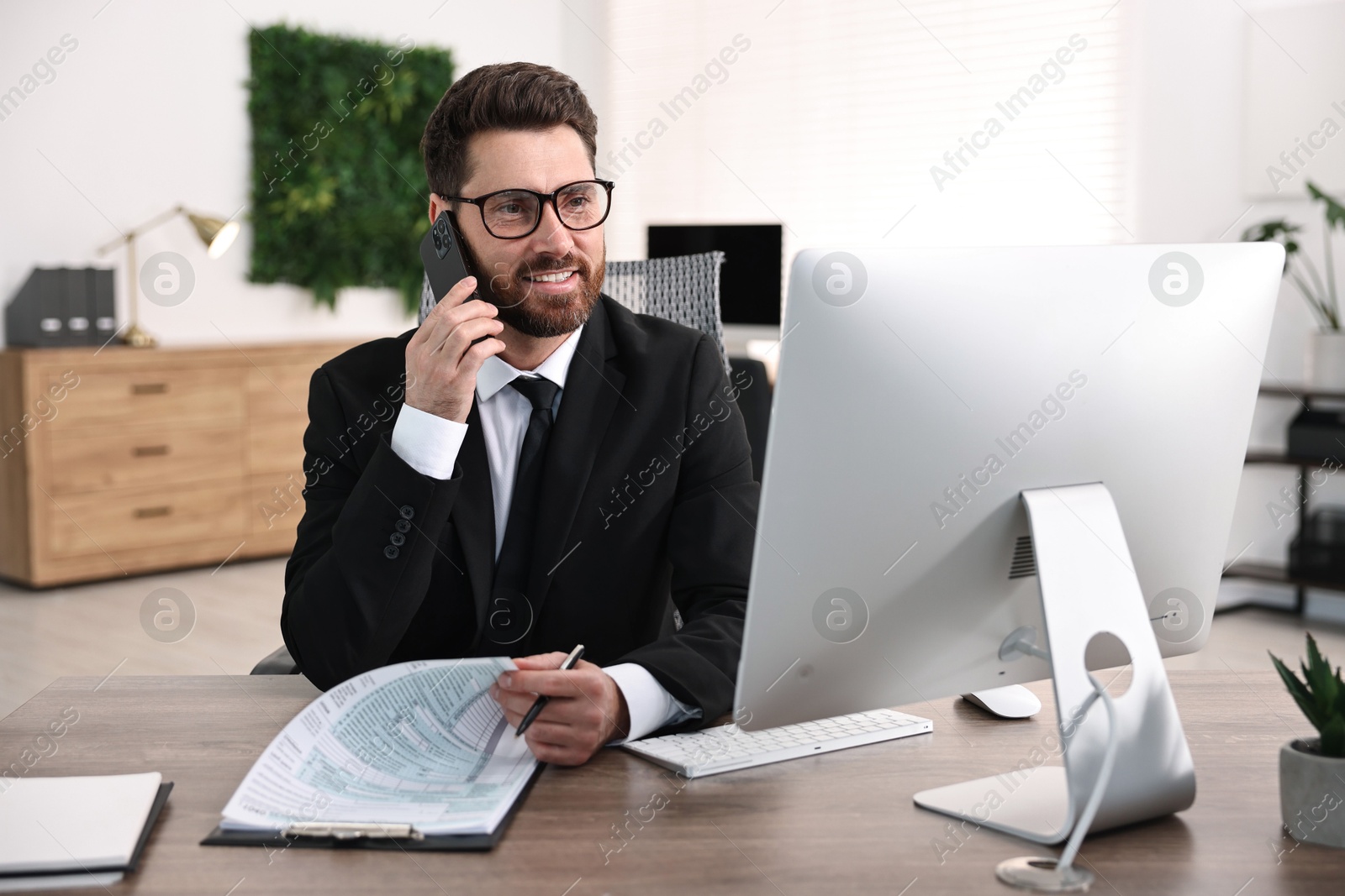 Photo of Man talking on smartphone while working at table in office