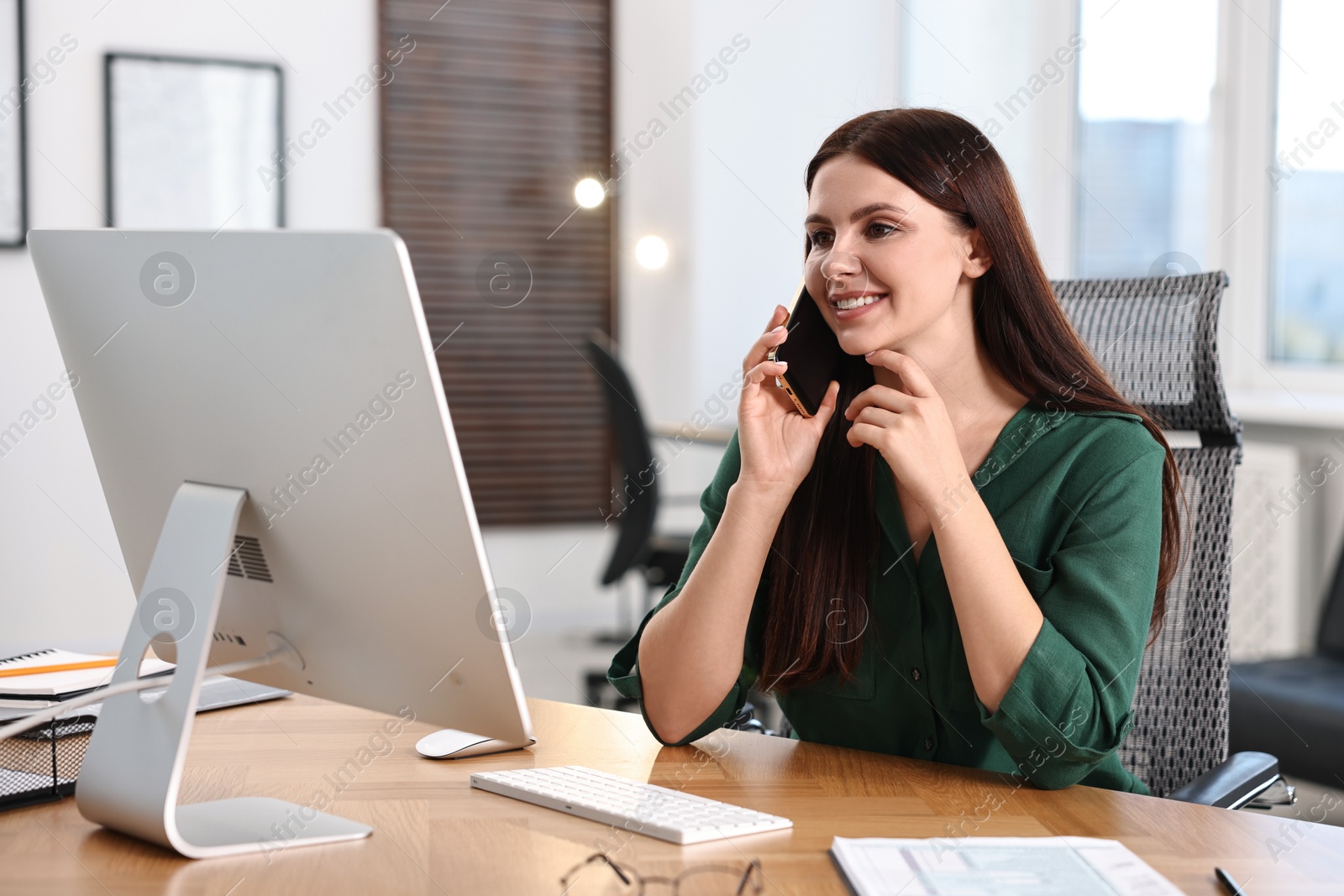 Photo of Woman talking on smartphone while working at table in office