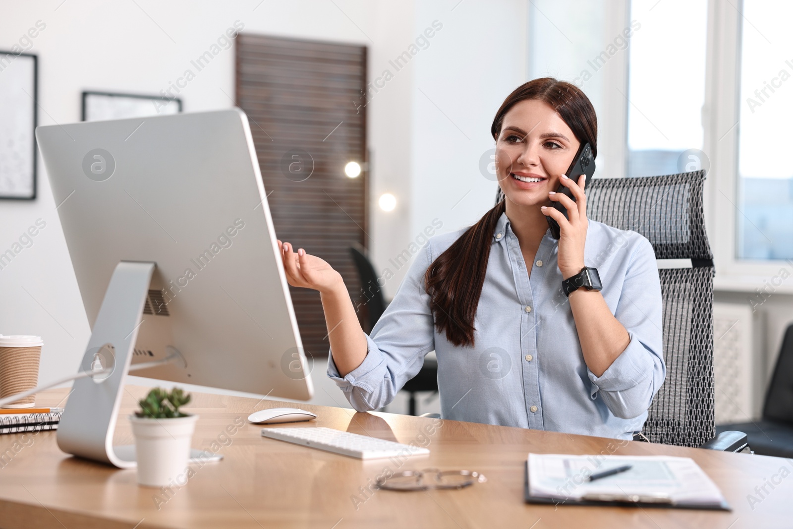 Photo of Woman talking on smartphone while working at table in office