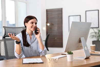 Photo of Woman talking on smartphone while working at table in office