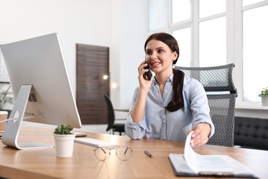 Photo of Woman talking on smartphone while working at table in office