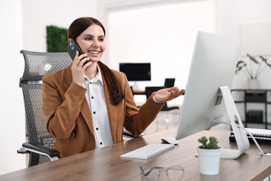 Photo of Woman talking on smartphone while working at table in office