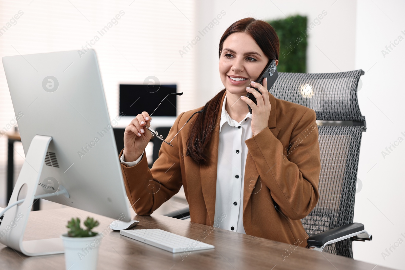 Photo of Woman talking on smartphone while working at table in office