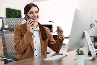 Photo of Woman talking on smartphone while working at table in office