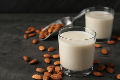 Photo of Fresh almond milk in glasses and nuts on dark grey table, closeup