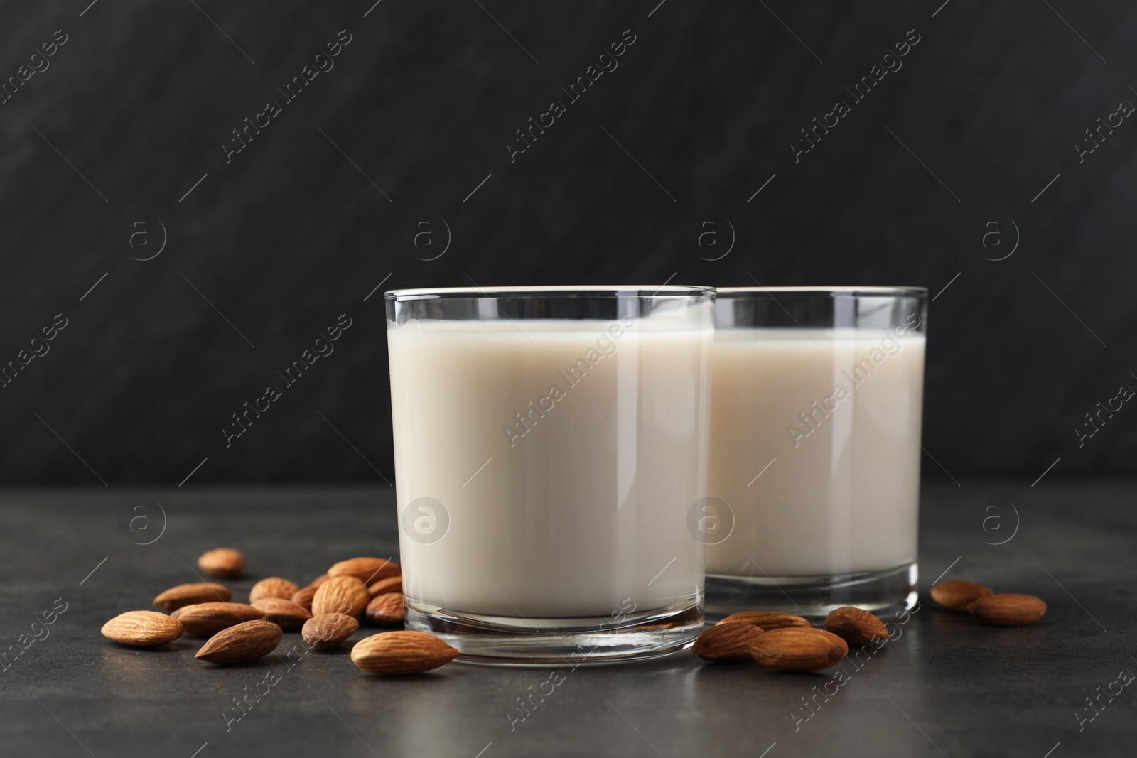 Photo of Fresh almond milk in glasses and nuts on dark grey table