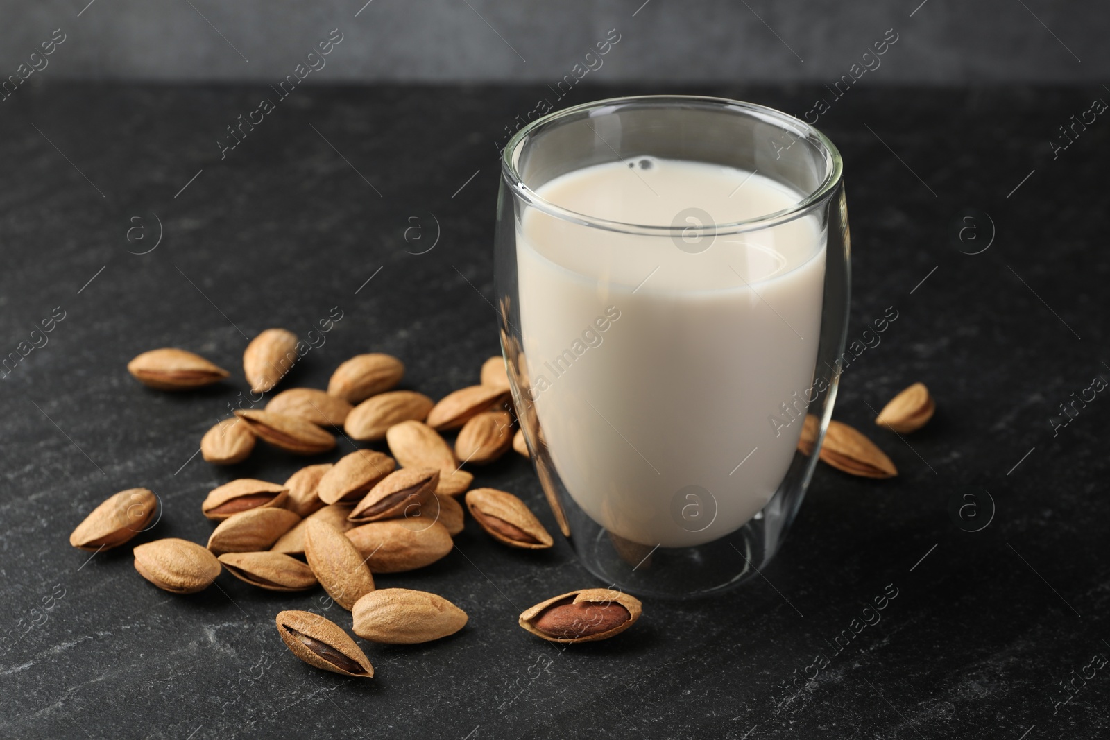 Photo of Fresh almond milk in glass and nuts on black table