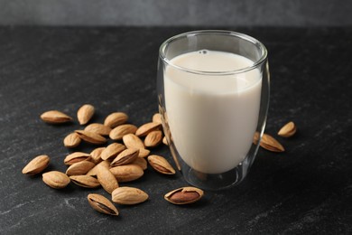 Photo of Fresh almond milk in glass and nuts on black table