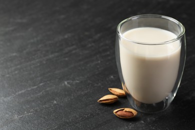 Photo of Fresh almond milk in glass and nuts on black table, closeup. Space for text