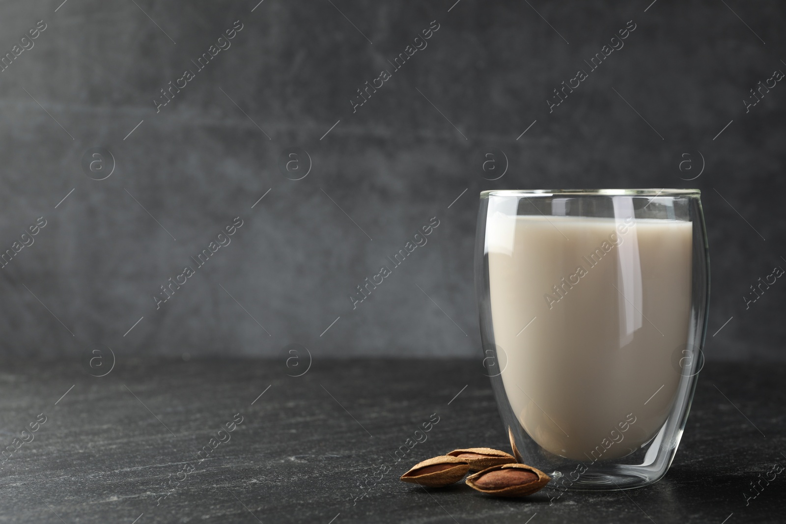 Photo of Fresh almond milk in glass and nuts on black table, space for text