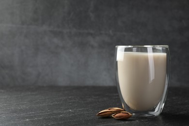 Photo of Fresh almond milk in glass and nuts on black table, space for text