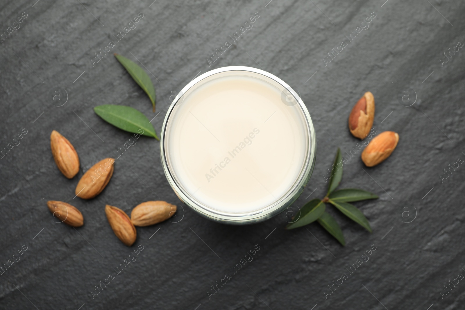 Photo of Fresh almond milk in glass, nuts and leaves on black table, top view