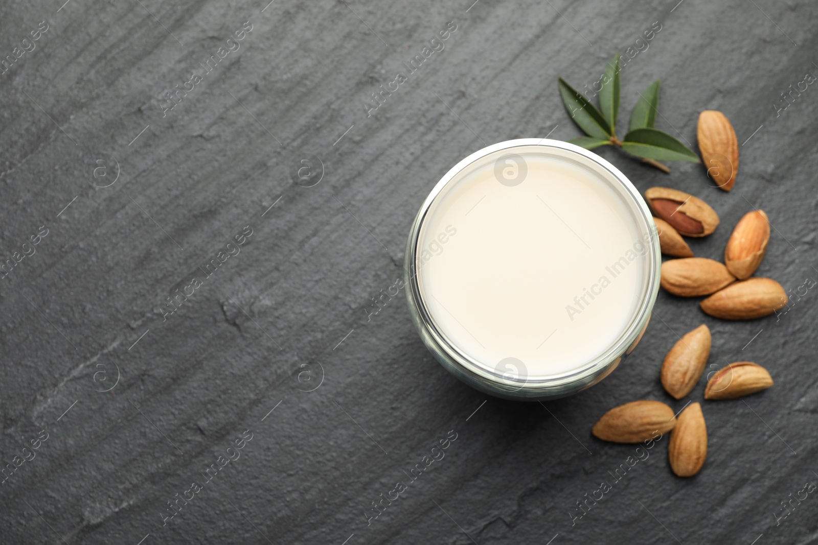 Photo of Fresh almond milk in glass, nuts and leaves on black table, top view. Space for text