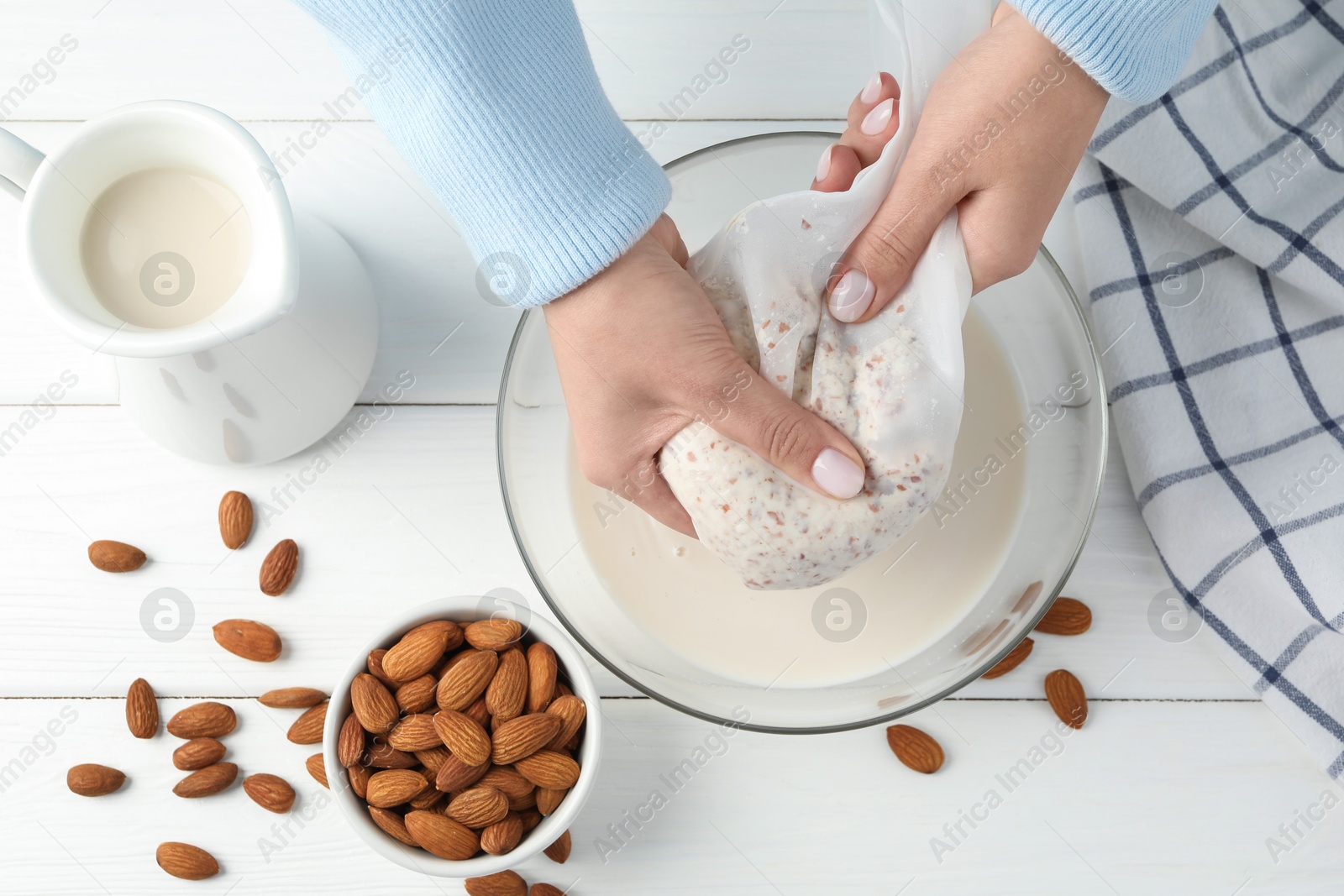 Photo of Woman making almond milk at white wooden table, top view