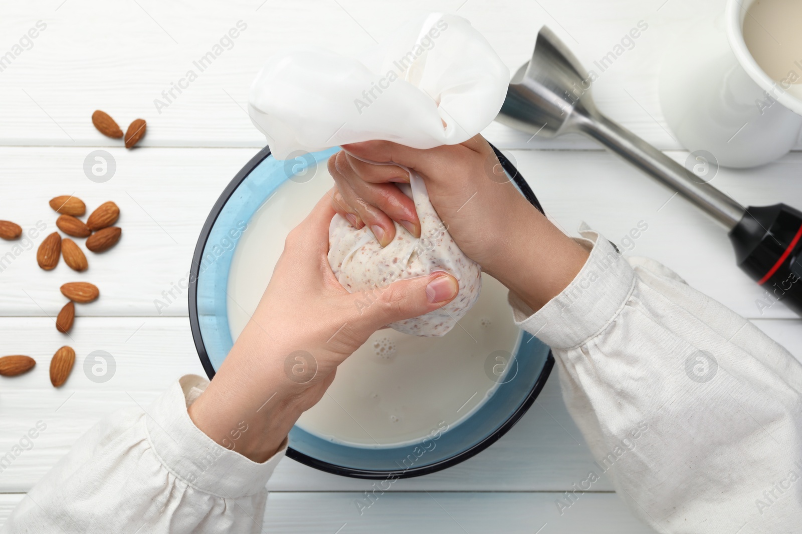 Photo of Woman making almond milk and nuts at white wooden table, top view