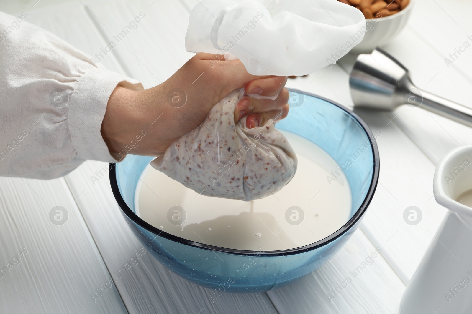 Photo of Woman making almond milk at white wooden table, closeup