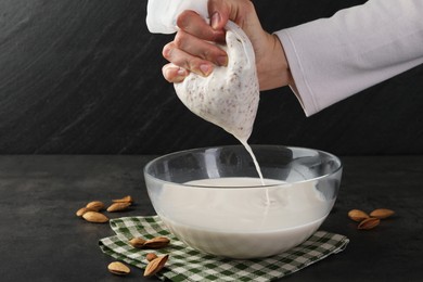 Photo of Woman making almond milk and nuts at black table, closeup