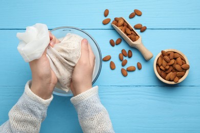 Photo of Woman making almond milk and nuts at light blue wooden table, top view