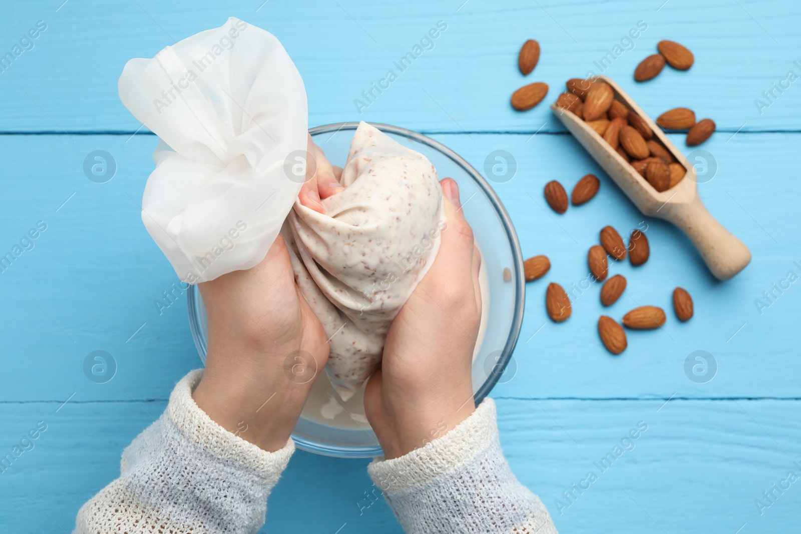 Photo of Woman making almond milk and nuts at light blue wooden table, top view